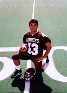 Lewis Nelson kneels on a football field with football and a helmet posing for the photo